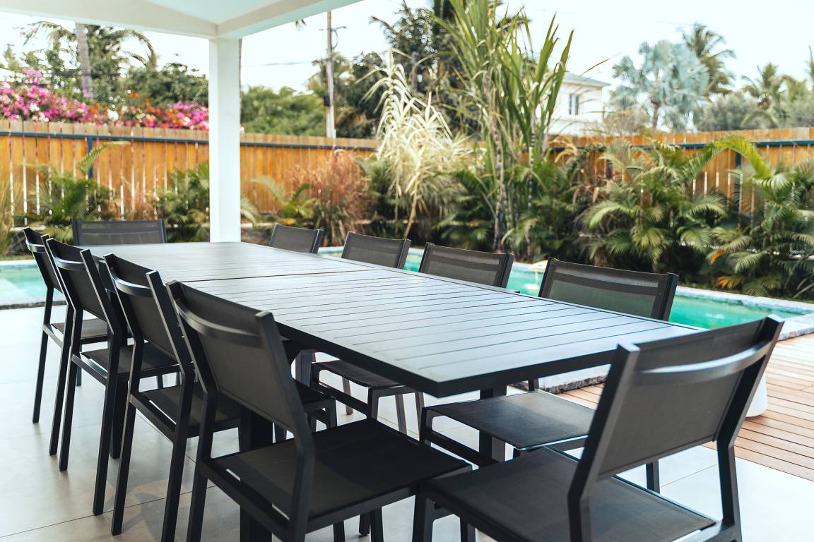 Grande table à manger extérieure au bord de la piscine sous la terrasse couverte