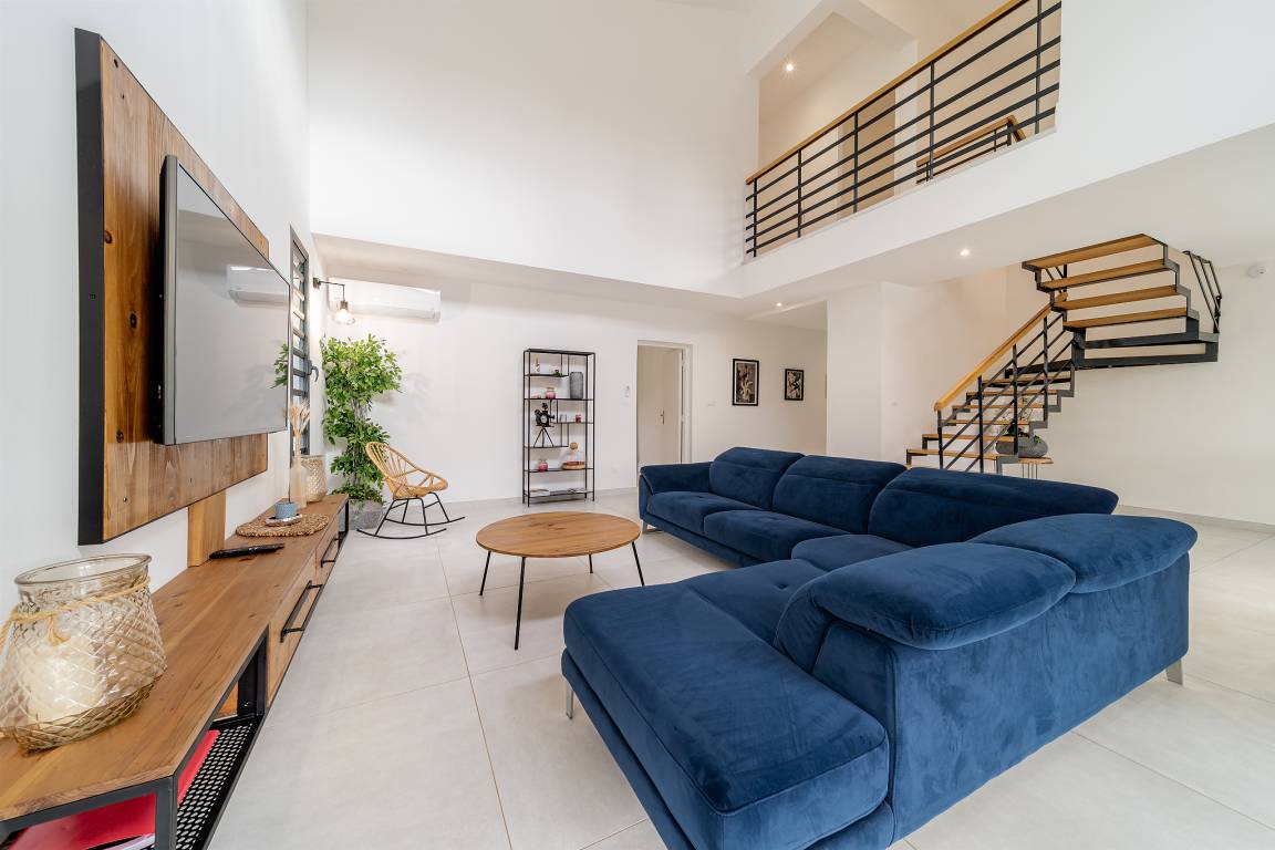 Vue du séjour avec canapé bleu, escalier en bois et métal et mezzanine