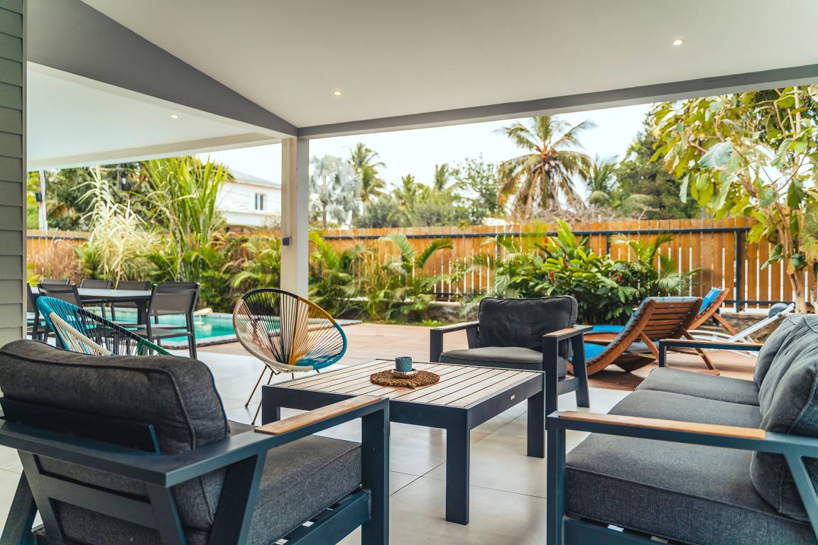 Salon de jardin sous la terrasse couverte avec fauteuils, canapé et vue sur le deck